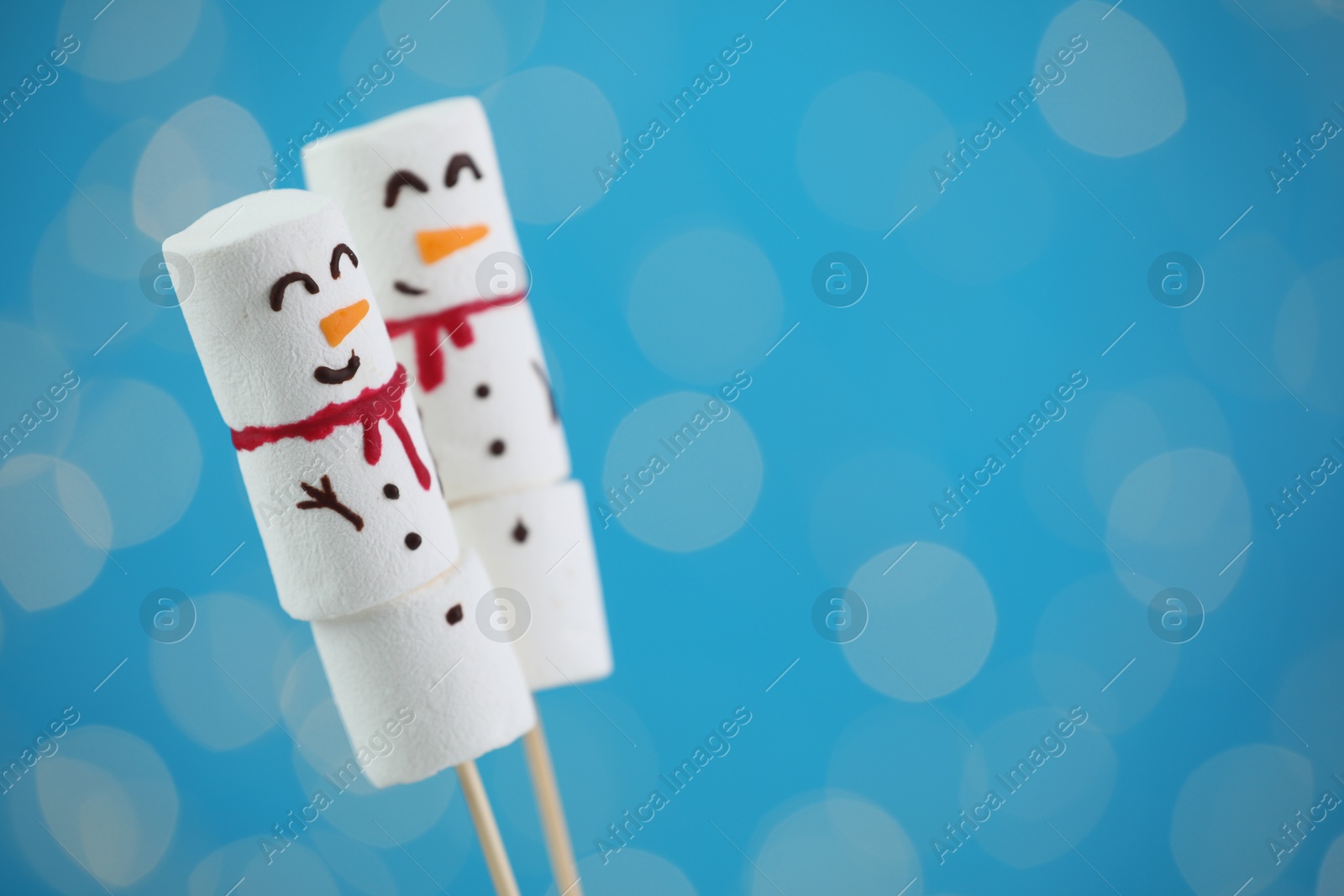 Photo of Funny snowmen made of marshmallows on blue background with blurred lights. Space for text