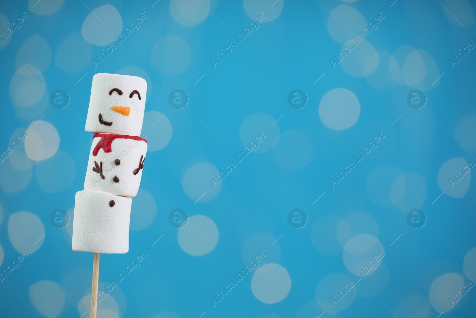 Photo of Funny snowman made of marshmallows on blue background with blurred lights. Space for text