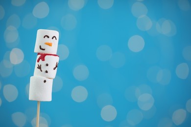 Photo of Funny snowman made of marshmallows on blue background with blurred lights. Space for text