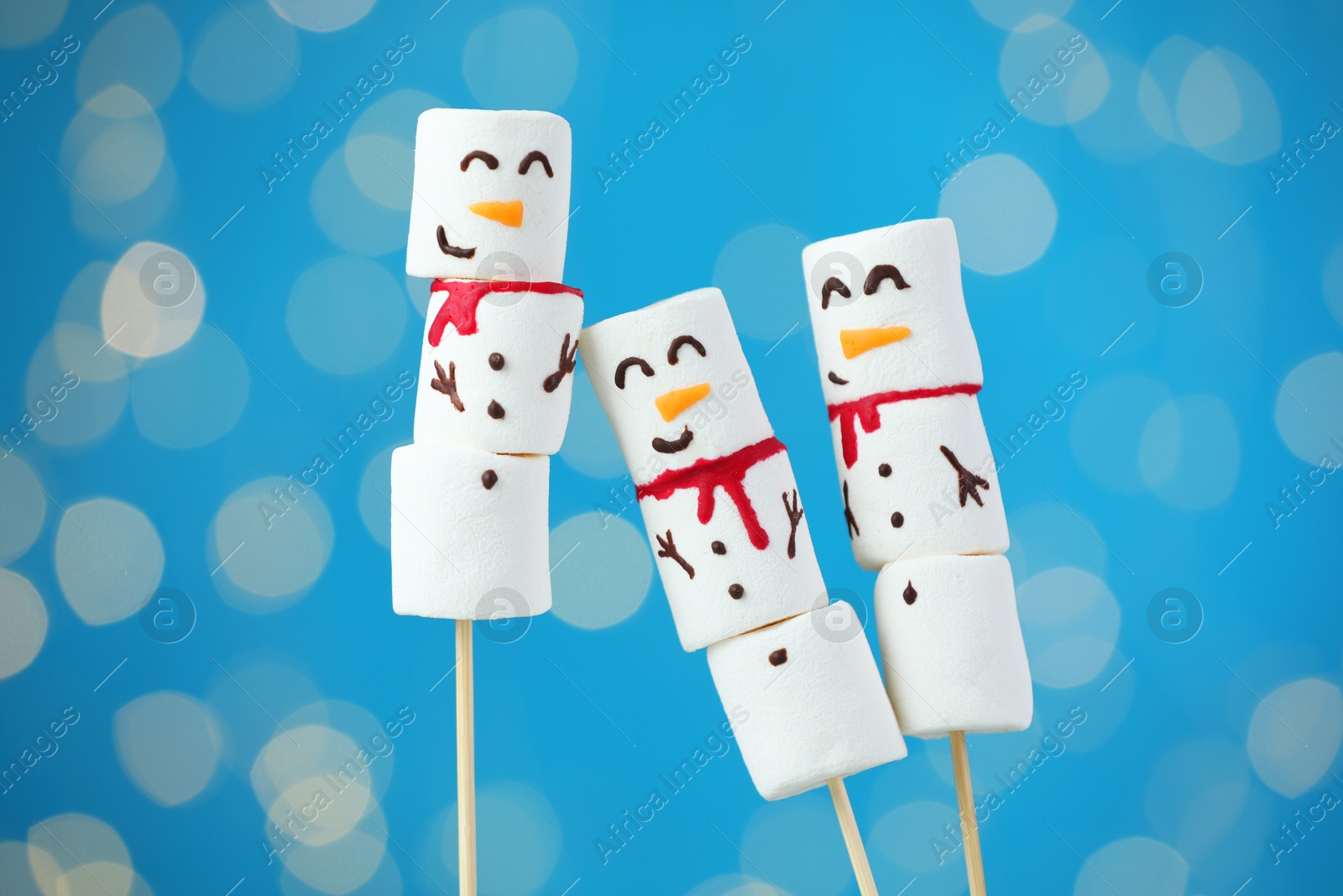 Photo of Funny snowmen made of marshmallows on blue background with blurred lights