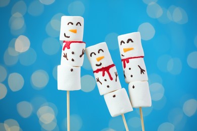 Photo of Funny snowmen made of marshmallows on blue background with blurred lights