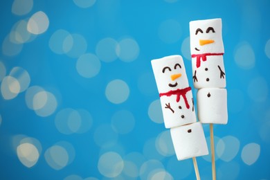 Photo of Funny snowmen made of marshmallows on blue background with blurred lights. Space for text