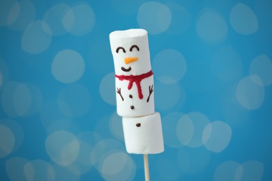 Photo of Funny snowman made of marshmallows on blue background with blurred lights