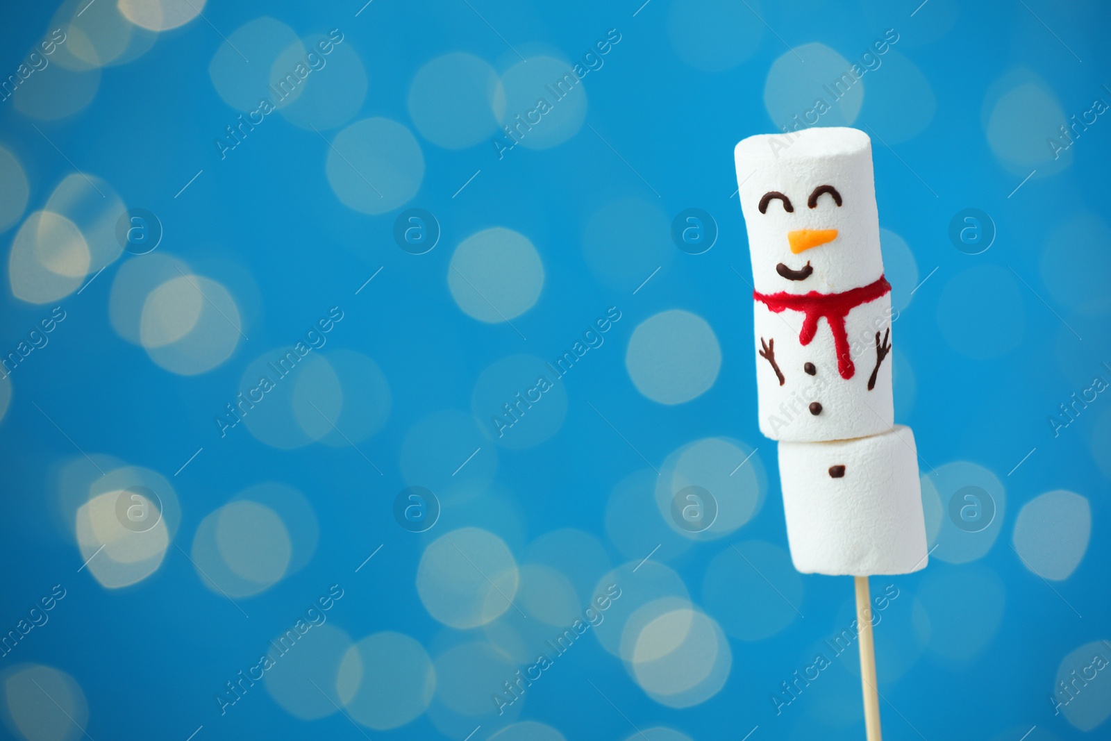 Photo of Funny snowman made of marshmallows on blue background with blurred lights. Space for text