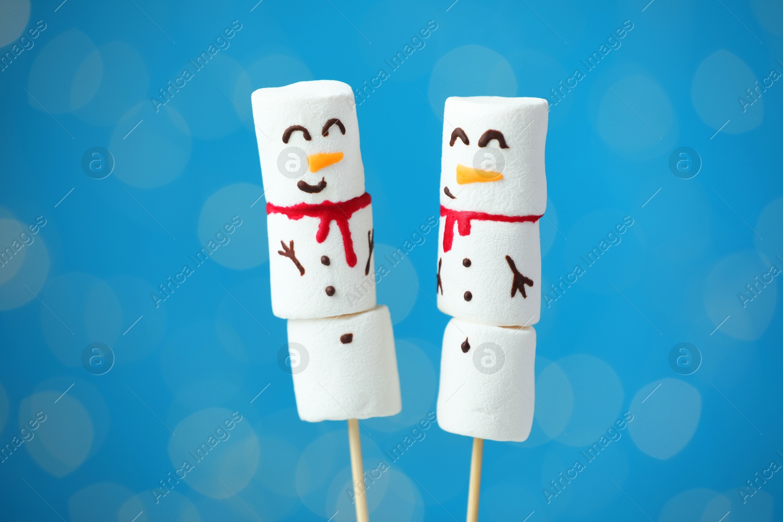 Photo of Funny snowmen made of marshmallows on blue background with blurred lights