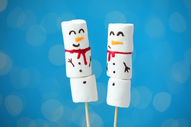 Photo of Funny snowmen made of marshmallows on blue background with blurred lights