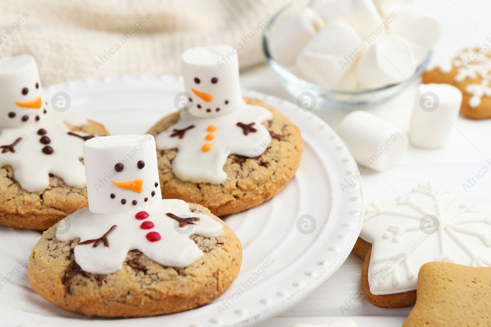 Photo of Delicious cookies with snowmen made of marshmallows on white table, closeup