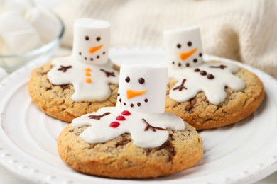 Photo of Delicious cookies with snowmen made of marshmallows on white table, closeup