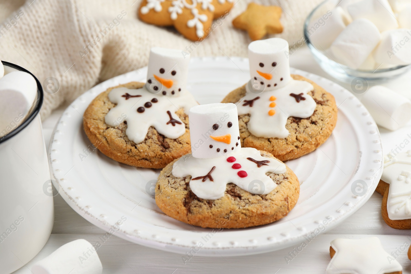 Photo of Delicious cookies with snowmen made of marshmallows on white table, closeup