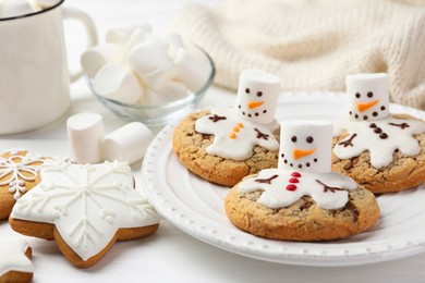 Photo of Delicious cookies with snowmen made of marshmallows on white table, closeup