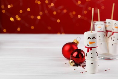 Photo of Funny snowmen made with marshmallows and Christmas decor on white wooden table, selective focus. Space for text