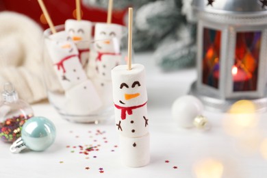 Photo of Funny snowmen made with marshmallows and Christmas decor on white table, selective focus