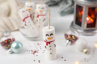 Photo of Funny snowmen made with marshmallows and Christmas decor on white table, selective focus