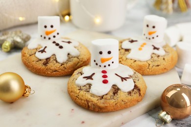 Photo of Delicious cookies with snowmen made of marshmallows on white table, closeup