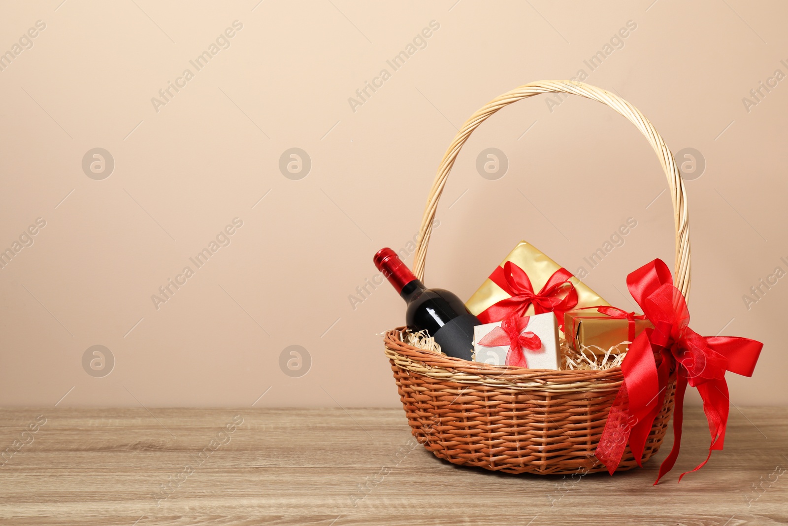 Photo of Wicker gift basket with wine on wooden table, space for text