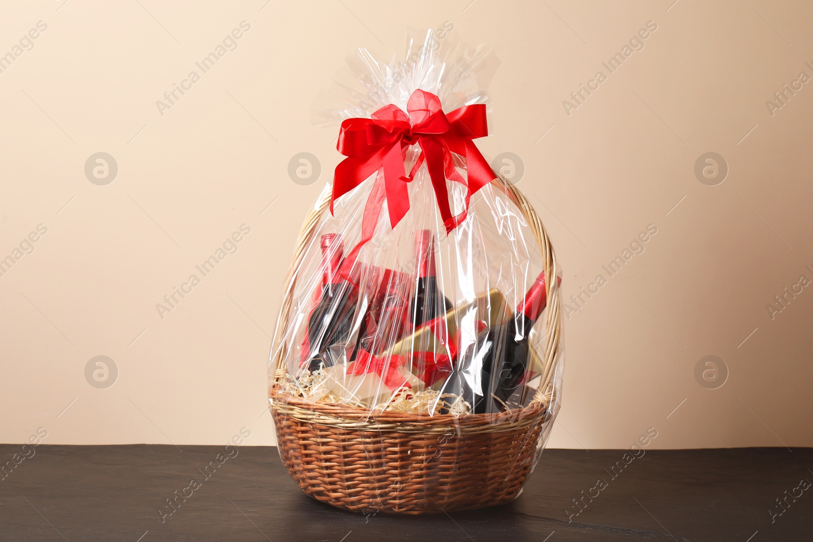 Photo of Wicker gift basket with wine on black textured table against beige background