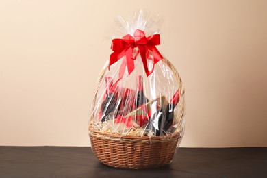 Wicker gift basket with wine on black textured table against beige background