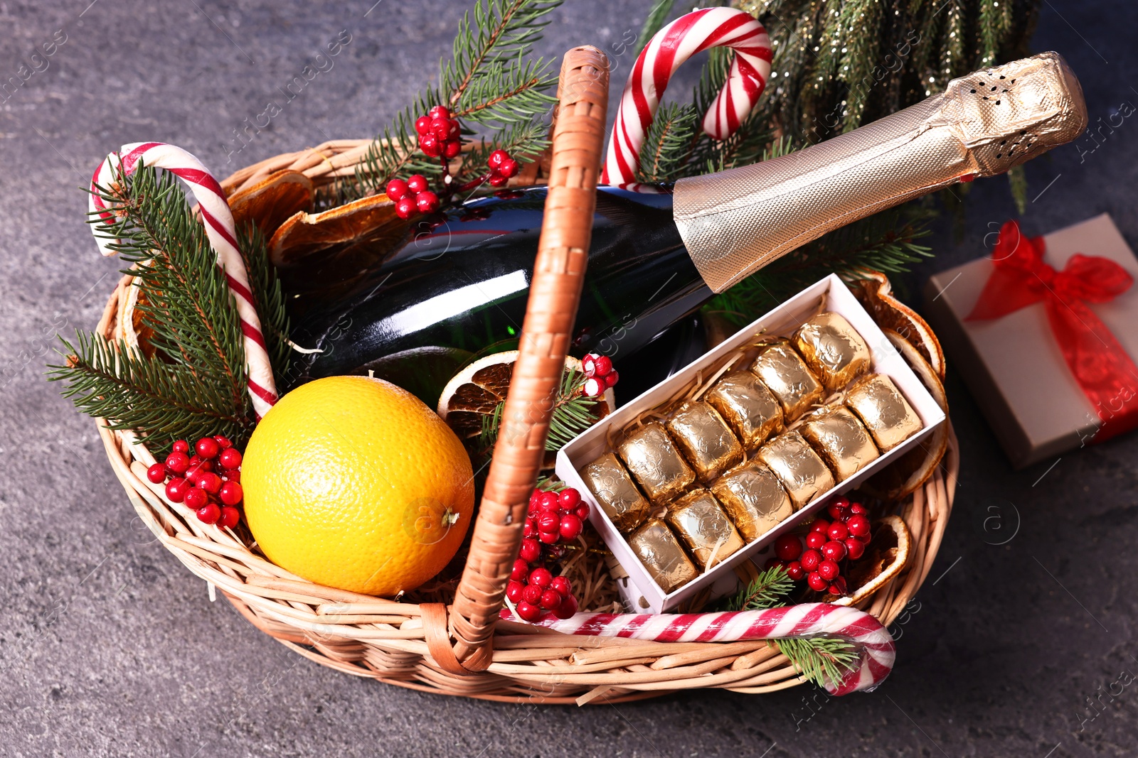 Photo of Wicker gift basket with sparkling wine and Christmas decor on grey textured table