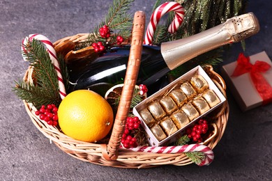 Wicker gift basket with sparkling wine and Christmas decor on grey textured table