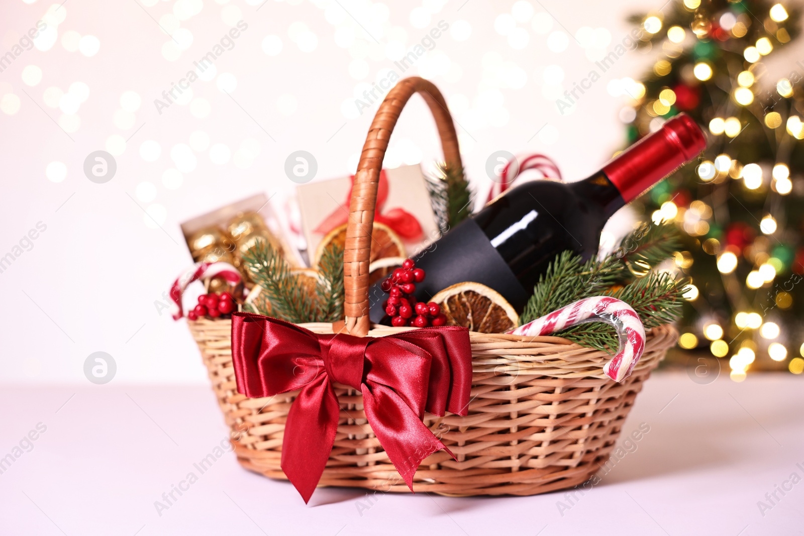 Photo of Wicker gift basket with wine and Christmas decor on light table