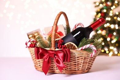 Photo of Wicker gift basket with wine and Christmas decor on light table