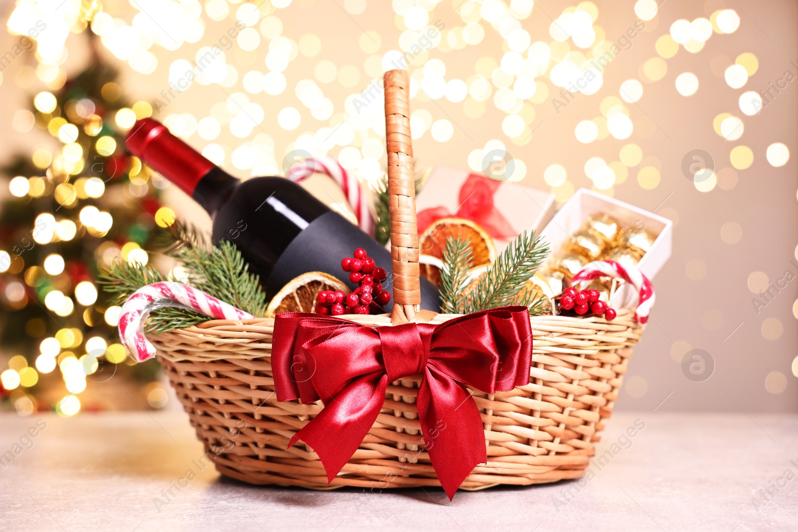 Photo of Wicker gift basket with wine and Christmas decor on light textured table