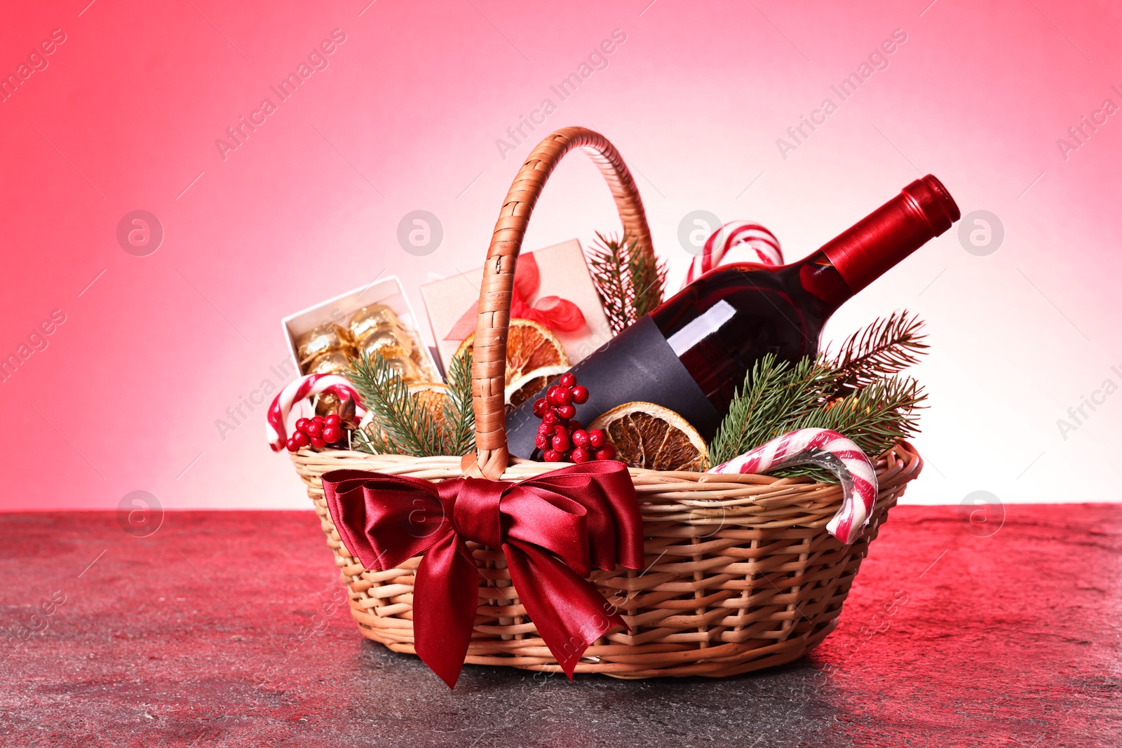 Photo of Wicker gift basket with wine and Christmas decor on grey textured table against color background