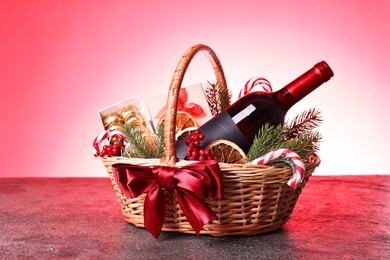 Wicker gift basket with wine and Christmas decor on grey textured table against color background