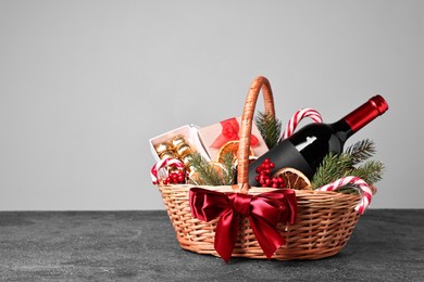 Wicker gift basket with wine and Christmas decor on grey textured table, space for text