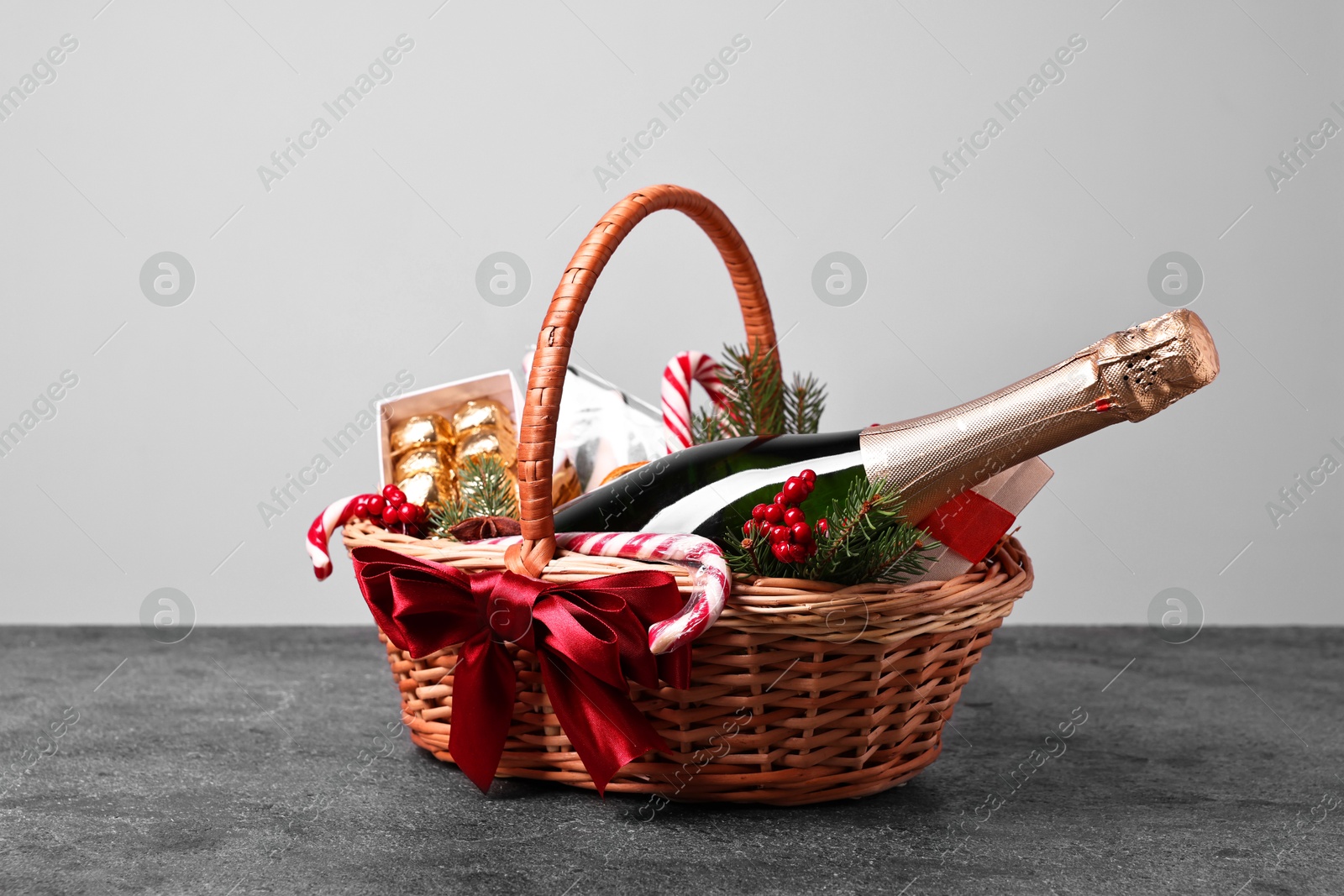 Photo of Wicker gift basket with sparkling wine and Christmas decor on grey textured table