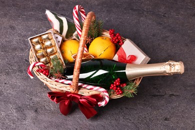 Wicker gift basket with sparkling wine and Christmas decor on grey textured table, above view