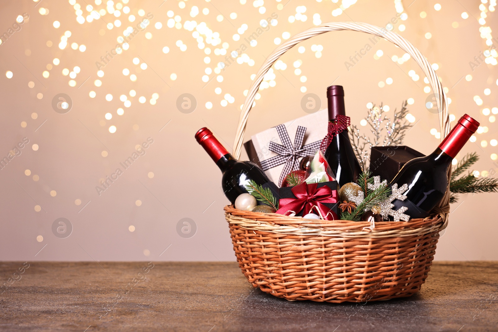 Photo of Wicker gift basket with wine and Christmas decor on grey textured table, space for text