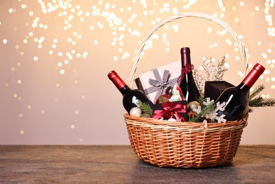 Wicker gift basket with wine and Christmas decor on grey textured table, space for text