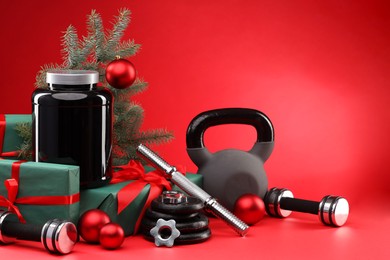 Photo of Dumbbells, kettlebell, container with supplement and Christmas decor on red background. Space for text