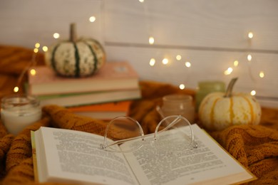 Photo of Open book, glasses and autumn decor on warm sweater, closeup