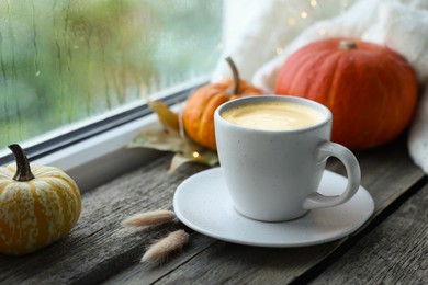 Photo of Cup of coffee and autumn decor on window sill, closeup