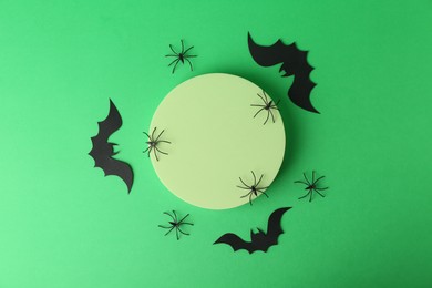 Photo of Halloween celebration. Podium, decorative bats and spiders on green background, flat lay. Space for text