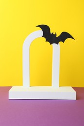 Photo of Halloween celebration. Podium and paper bat on purple table against yellow background. Space for text