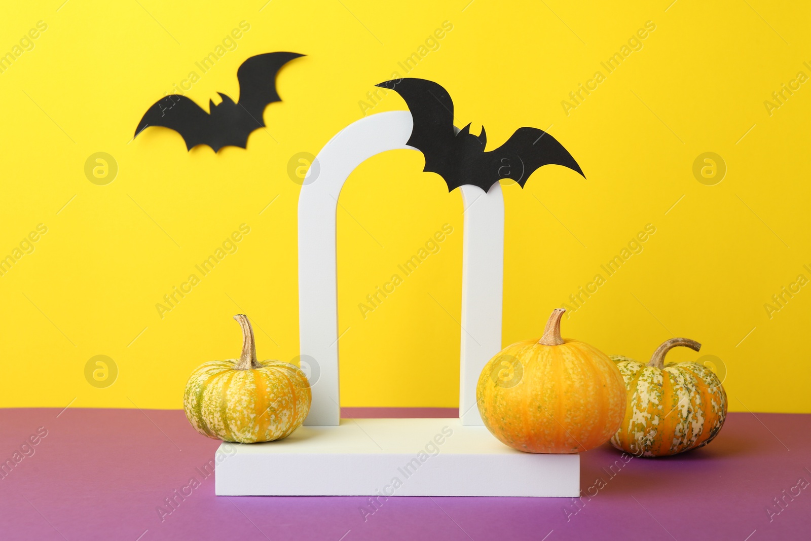 Photo of Presentation of product. Podium and Halloween decor on purple table against yellow background. Space for text