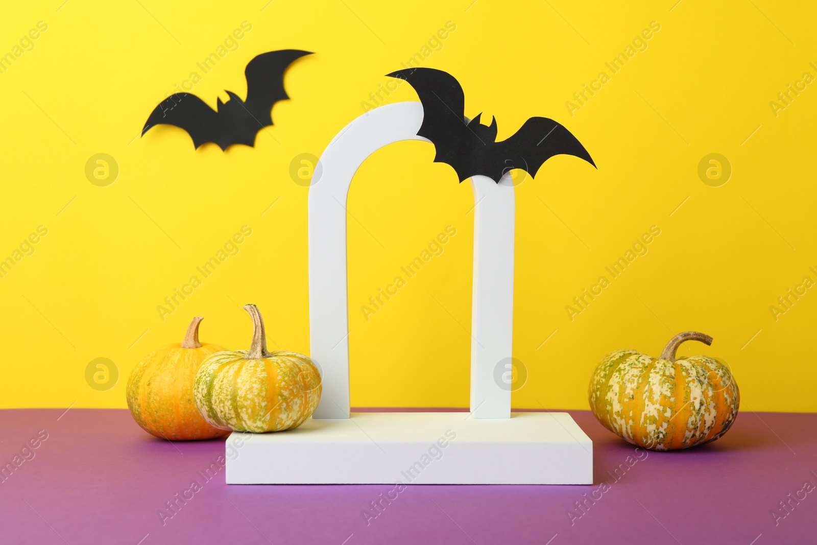 Photo of Presentation of product. Podium and Halloween decor on purple table against yellow background. Space for text