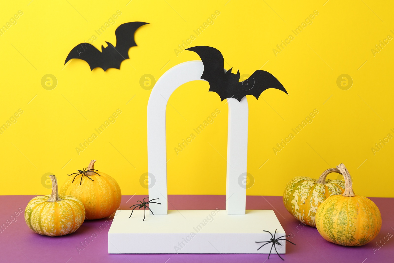 Photo of Presentation of product. Podium and Halloween decor on purple table against yellow background. Space for text