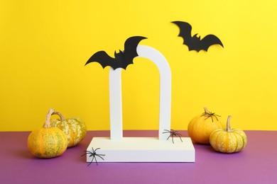 Photo of Presentation of product. Podium and Halloween decor on purple table against yellow background. Space for text