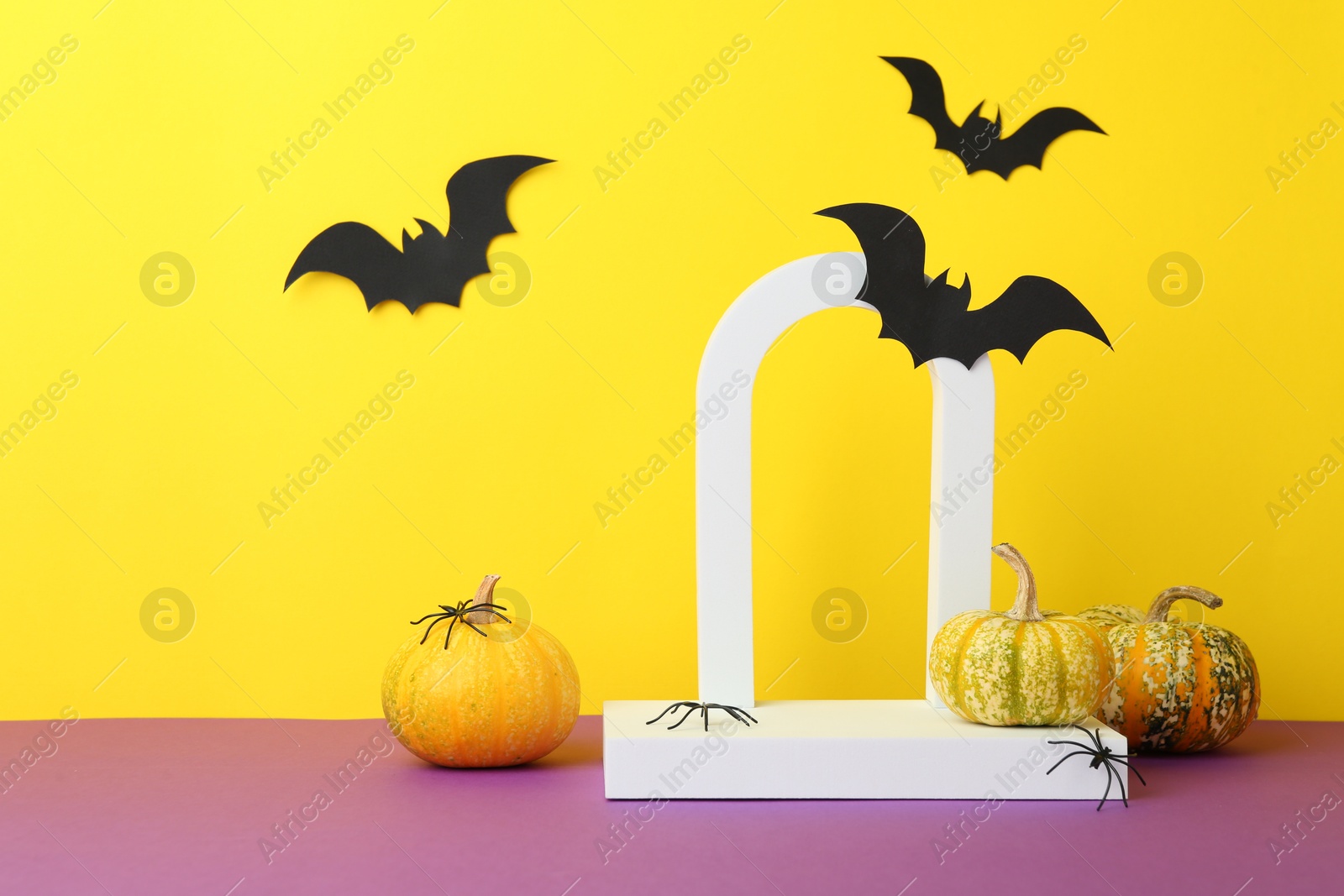 Photo of Presentation of product. Podium and Halloween decor on purple table against yellow background. Space for text