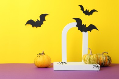 Presentation of product. Podium and Halloween decor on purple table against yellow background. Space for text