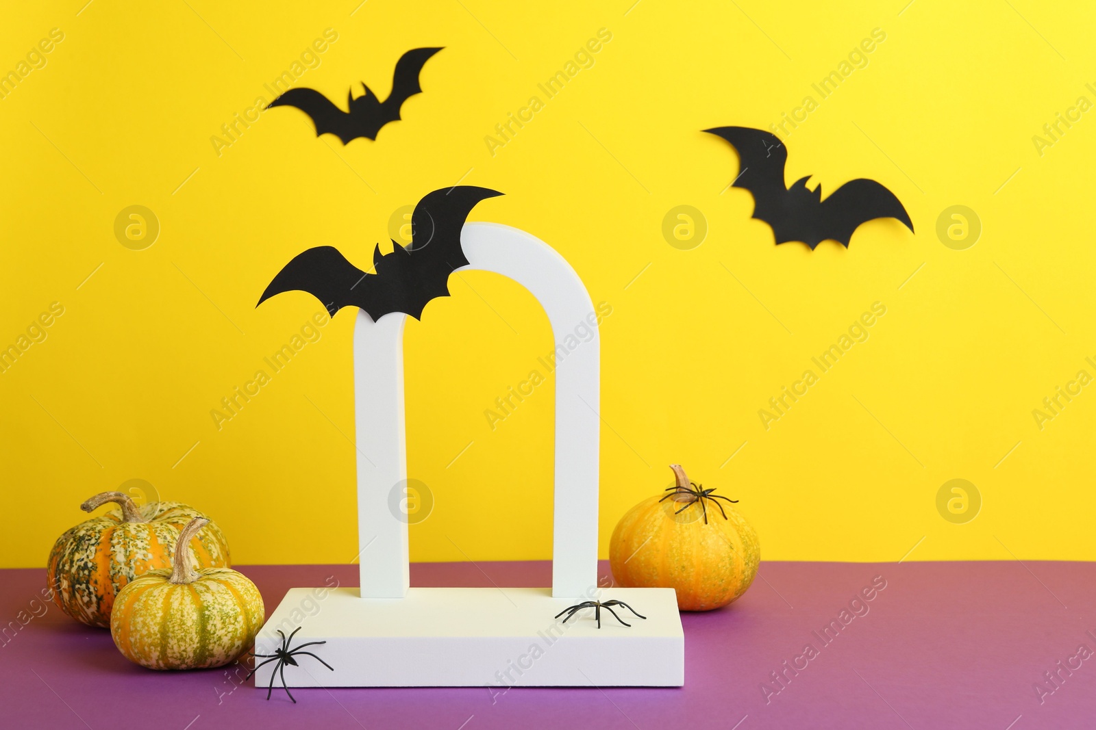 Photo of Presentation of product. Podium and Halloween decor on purple table against yellow background. Space for text