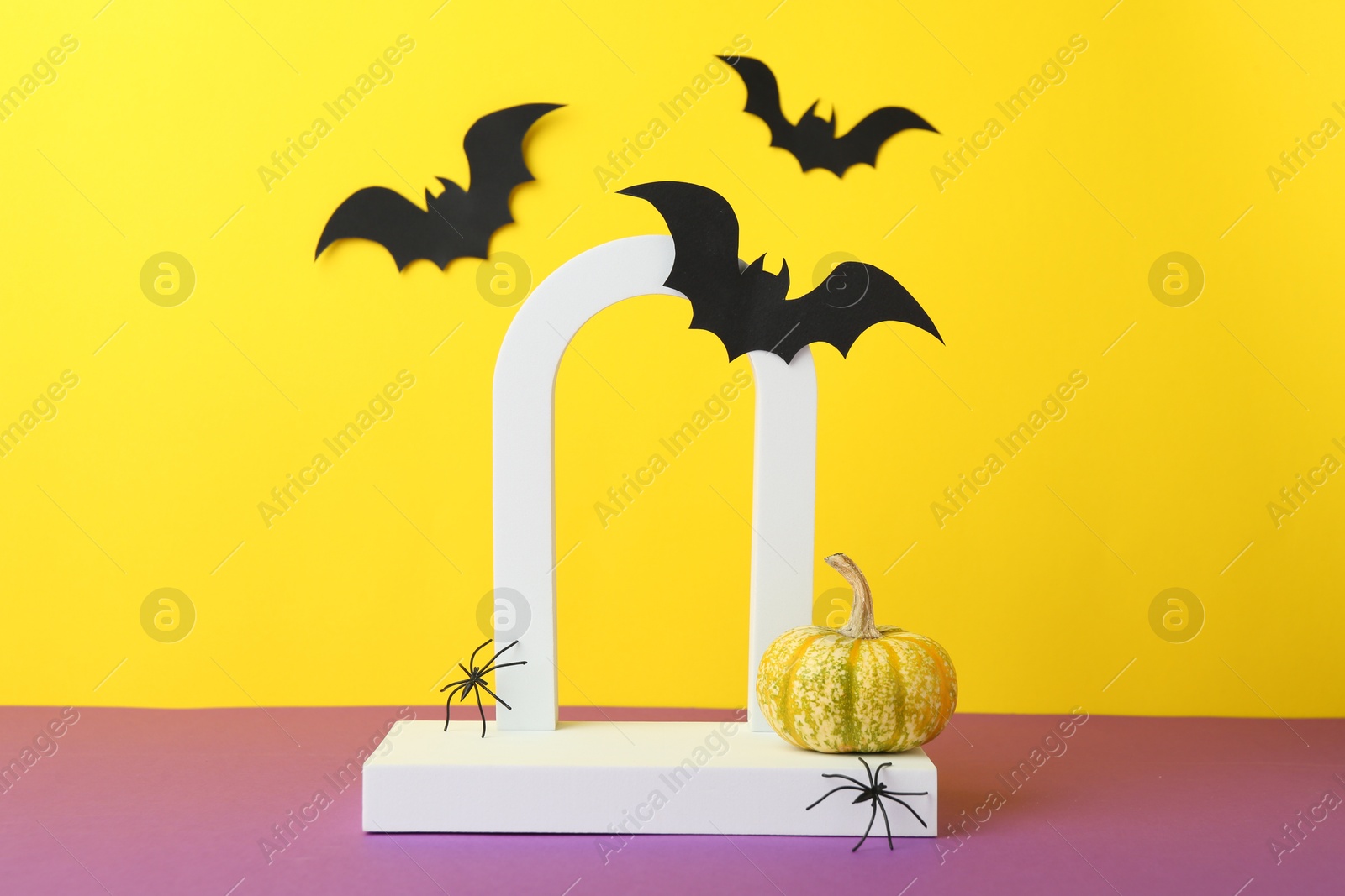 Photo of Presentation of product. Podium and Halloween decor on purple table against yellow background. Space for text