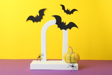 Photo of Presentation of product. Podium and Halloween decor on purple table against yellow background. Space for text