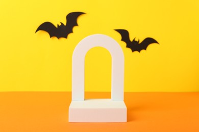 Photo of Halloween celebration. Podium and paper bats on orange table against yellow background, space for text