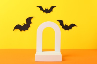 Photo of Halloween celebration. Podium and paper bats on orange table against yellow background, space for text