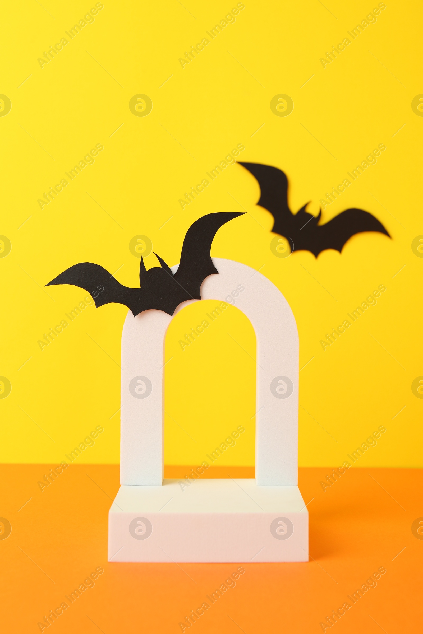 Photo of Halloween celebration. Podium and paper bats on orange table against yellow background, space for text